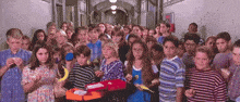 a large group of children are standing in a hallway holding lunch boxes
