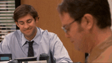 a man in a blue shirt and tie is smiling while another man looks on