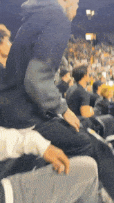 a man in a black hoodie sits in the stands at a sports game