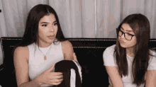 two girls are sitting on a couch one wearing glasses