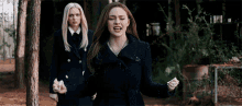 two women are standing next to each other in a forest and one of them is screaming .