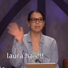 a woman wearing glasses and a denim shirt is sitting in front of a laptop .