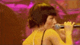 a woman is singing into a microphone with a pink background .