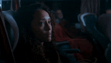a woman with curly hair is sitting in a dark room with her eyes closed