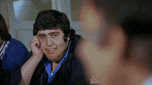 a man in a blue shirt is sitting with his hand on his ear