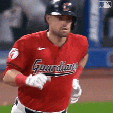 a man in a red guardians jersey is running on a baseball field .