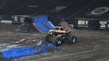 a monster truck is driving down a dirt track with a sign that says the video game in the background