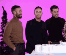 three men standing next to a box of toilet paper on a pink background