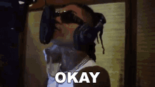 a woman wearing headphones and sunglasses is singing into a microphone and saying `` okay '' .