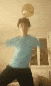 a person in a blue shirt is dancing in a room with a disco ball hanging from the ceiling