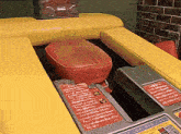 a red cushion is sitting on top of a yellow table next to a brick wall ..