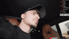a man wearing a hat is sitting in a car with the number 39,381,242 on the screen behind him
