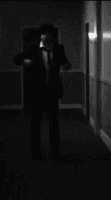 a black and white photo of a man in a tuxedo walking down a hallway .