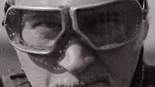 a close up of a man 's face wearing goggles and a mustache