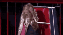 a woman in a sequined jacket is standing in front of a red chair on a stage .