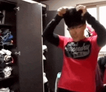 a man wearing a red superdry shirt adjusts his hat