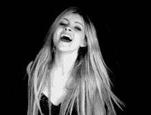 a black and white photo of a woman with long blonde hair laughing with her mouth open .