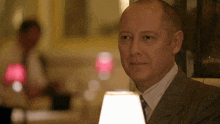 a bald man in a suit and tie looks at a lamp
