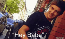 a young man leaning against a brick wall with the words " hey babe " above him
