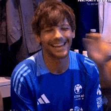 a man wearing a blue soccer aid shirt smiles for the camera