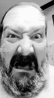 a black and white photo of a man with a beard and mustache making a funny face .