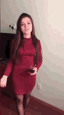 a woman in a red dress is standing in a room holding a glass of tea .