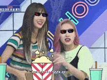 two girls wearing sunglasses are standing next to a popcorn bucket
