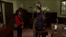 a woman in a red jacket stands in a room with a statue of jesus on the wall
