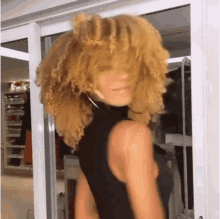 a woman with blonde curly hair is wearing a black tank top