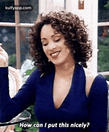 a woman with curly hair is sitting at a table and smiling while holding a glass of wine .