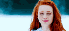 a woman with red hair is standing in the snow with her eyes closed and a sad look on her face .