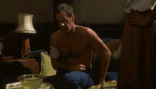 a shirtless man sits on a couch with a lamp on