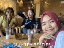 three women are sitting at a table with milk tea cups