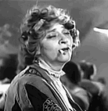 a black and white photo of a woman smoking a cigarette in a crowd .
