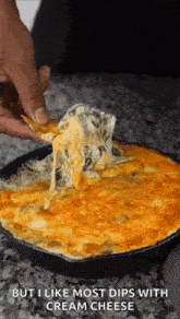 a person is dipping a tortilla chip into a dip with cream cheese .