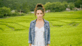 a woman in a white dress and denim jacket is standing in a field