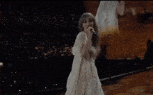 a woman in a white dress singing into a microphone with the words ' cause it was never mine ' on the bottom right