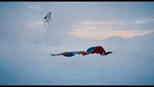 a man in a superman costume is laying in the snow with his mouth wide open