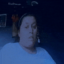 a woman wearing a headband and a white shirt is sitting in a dark room looking at the camera .