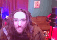 a man with long hair and glasses is sitting in front of a microphone .