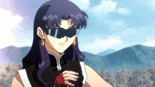 a woman wearing sunglasses and earrings stands in front of a mountain range