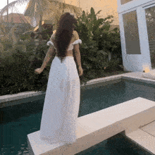 a woman in a white dress is standing in front of a pool