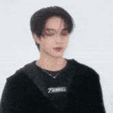 a young man wearing a black shirt that says painkill is standing in front of a white wall .