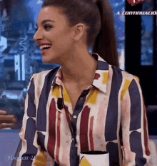 a woman in a striped shirt is smiling and holding a cup in front of a sign that says a continuacion