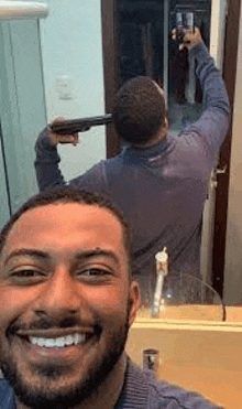 a man is taking a selfie with a gun in front of a mirror in a bathroom .