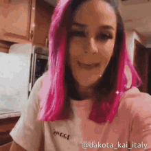 a woman with pink hair is taking a selfie in a kitchen .