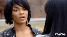 two women are standing next to each other and looking at each other . one of the women is wearing hoop earrings .