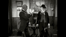 a black and white photo of two men standing next to each other in a room with a sign that says sochev