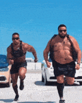 two muscular men are running in a parking lot with cars in the background