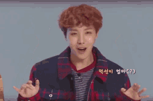 a young man in a plaid shirt is making a funny face with his hands in the air
